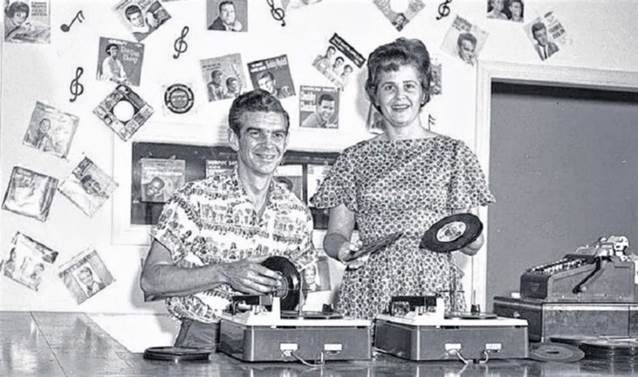 A person and person standing next to a record player

Description automatically generated with medium confidence
